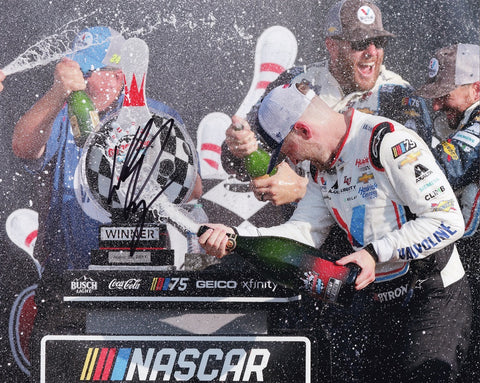 This autographed 2023 William Byron #24 WATKINS GLEN WIN NASCAR photo immortalizes the jubilant moment as Byron stands in Victory Lane, sprayed with champagne after his triumphant victory at Watkins Glen International.