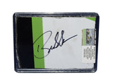 Displayed autographed Bubba Wallace #23 DraftKings Racing composite NASCAR sheet metal from the 2023 Loudon car with visible racing wear. Housed inside a protective plastic toploader, this trading-card-size collectible makes a great gift for Bubba Wallace fans and motorsports memorabilia collectors.