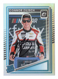 Front view of an autographed Connor Zilisch 2025 Donruss Optic Racing Rated Rookie Silver Prizm NASCAR trading card featuring the rising racing star. This signed rookie collectible showcases the distinctive reflective Silver Prizm finish and includes a Certificate of Authenticity, making it an exciting addition to any NASCAR trading card collection.